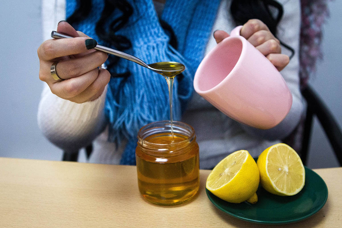 Person löffelt Honig in eine Teetasse. Honig kann bei der Behandlung von Husten helfen.
